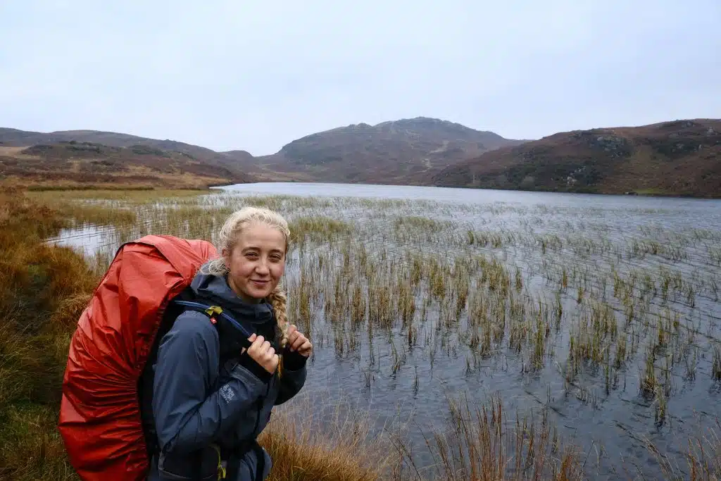 Female backpacker hiking past lake and showing what to wear hiking in the rain