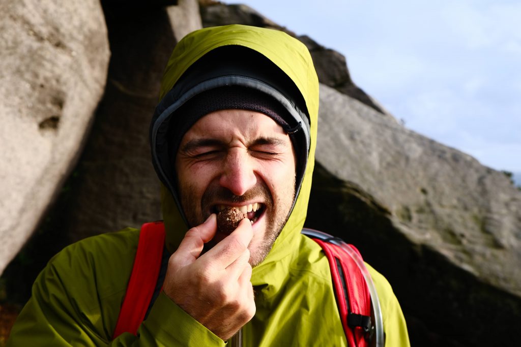 Man taking bite of vegan energy ball on hiking trail