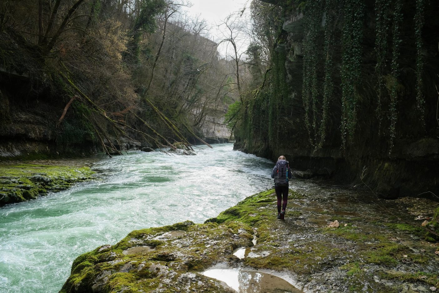 Girl walking with backpack next to large river