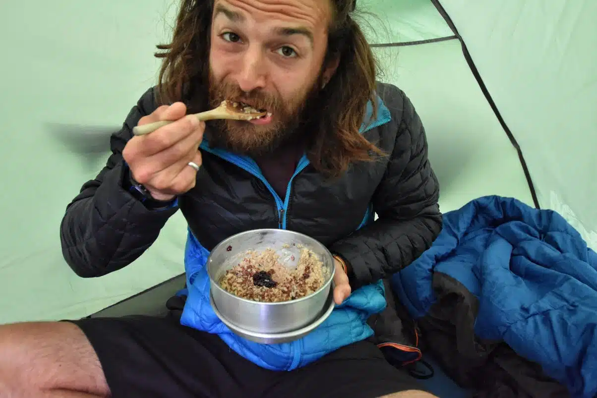 Man eating breakfast from pan in tent