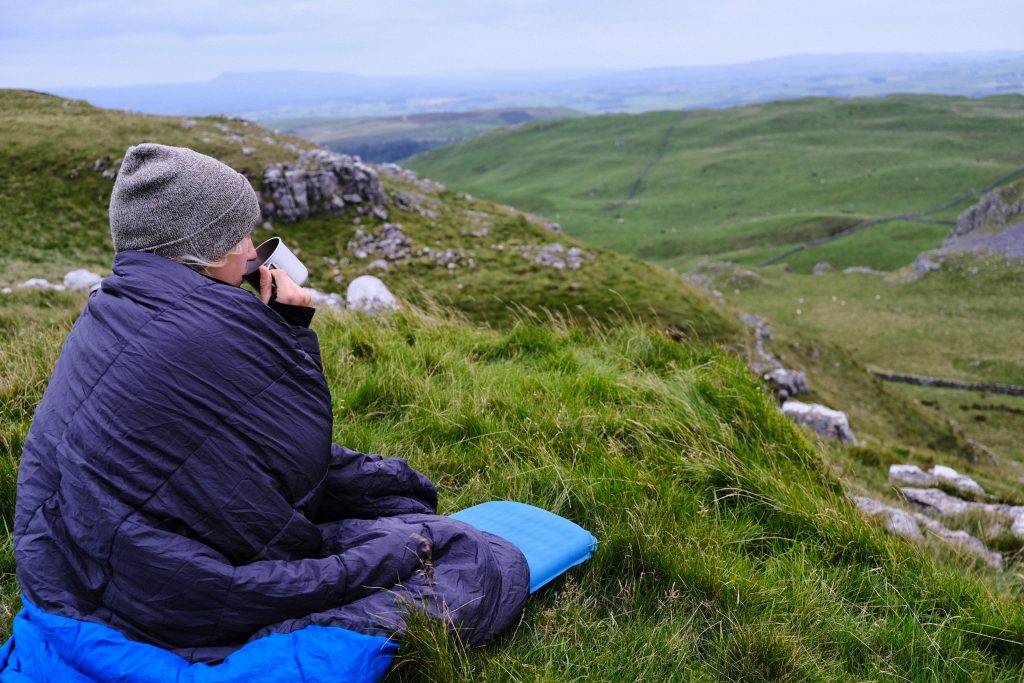 Girl sitting in sleeping bag on hillside 