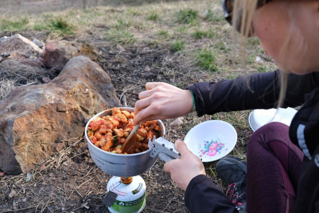 Girl stirring vegan peanut butter curry on camp stove 