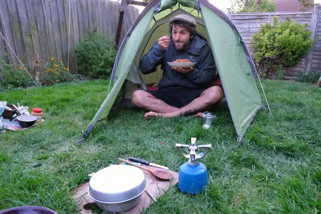Man eating peanut curry in front of tent 